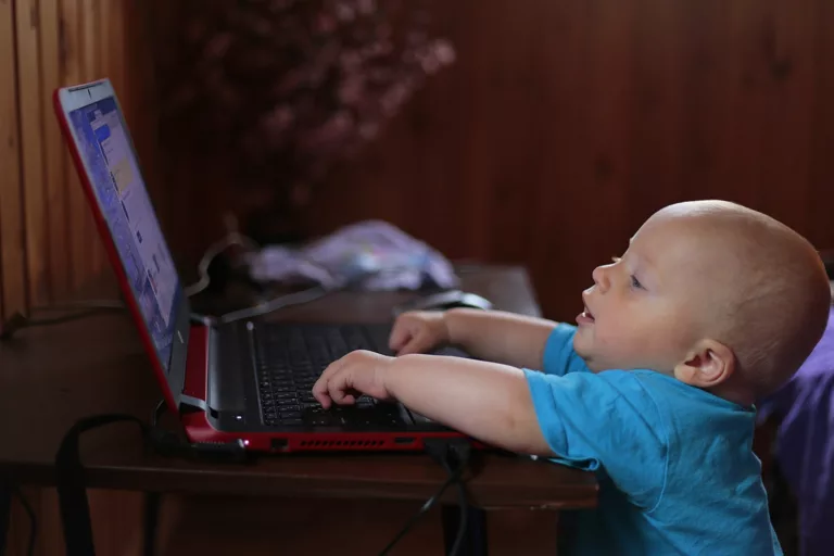 boy wearing blue t shirt using black laptop computer in a dim lighted scenario