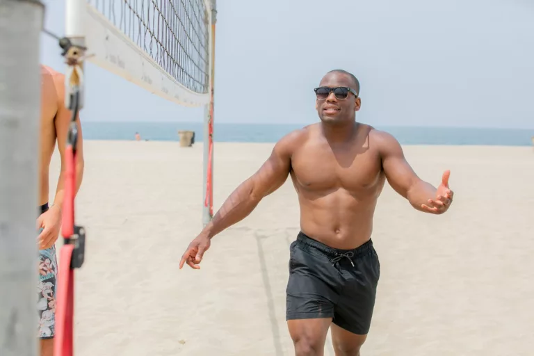 athletic man walking along beach volleyball net and gesturing