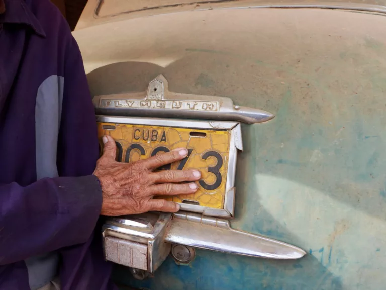 hand of elderly man touching licence plate on car