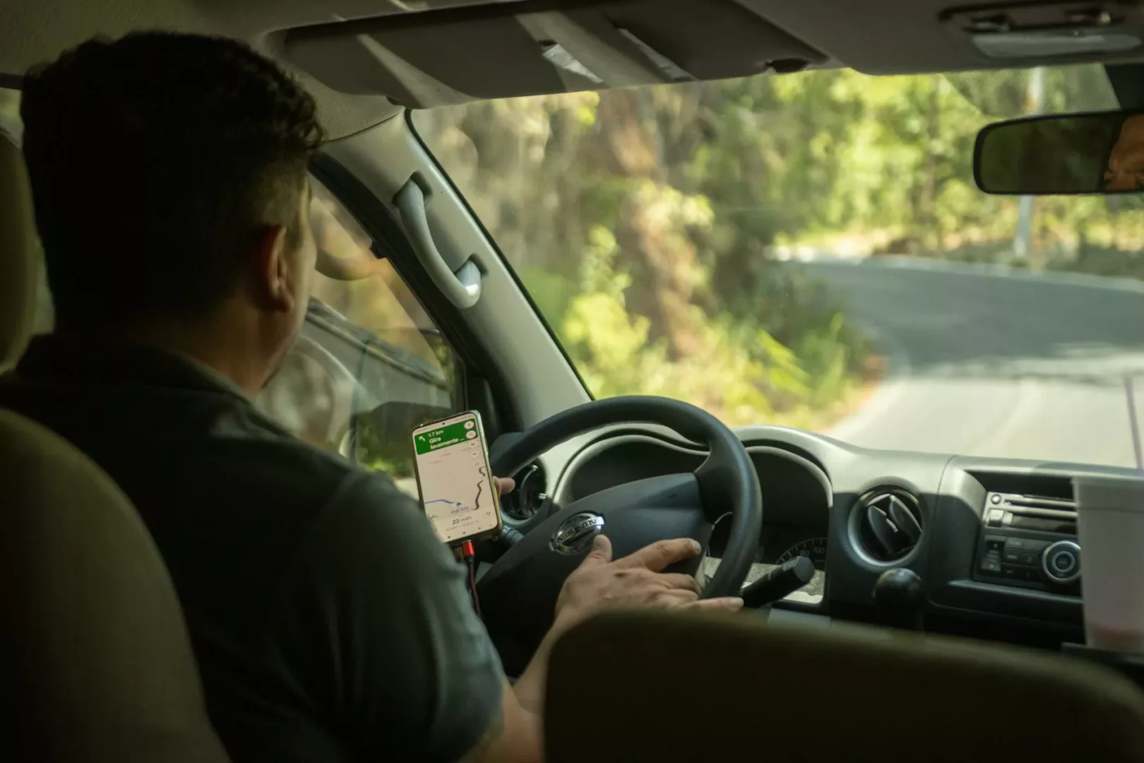 man in black polo shirt driving car using a mobile app for navigational aid