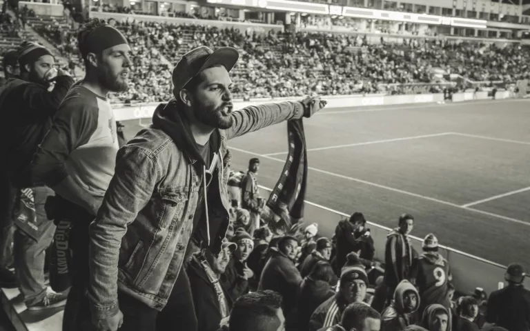 monochrome photo of man wearing jacket pointing finger at stadium