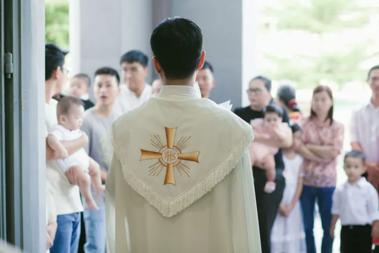 A priest stands in front of a crowd of people