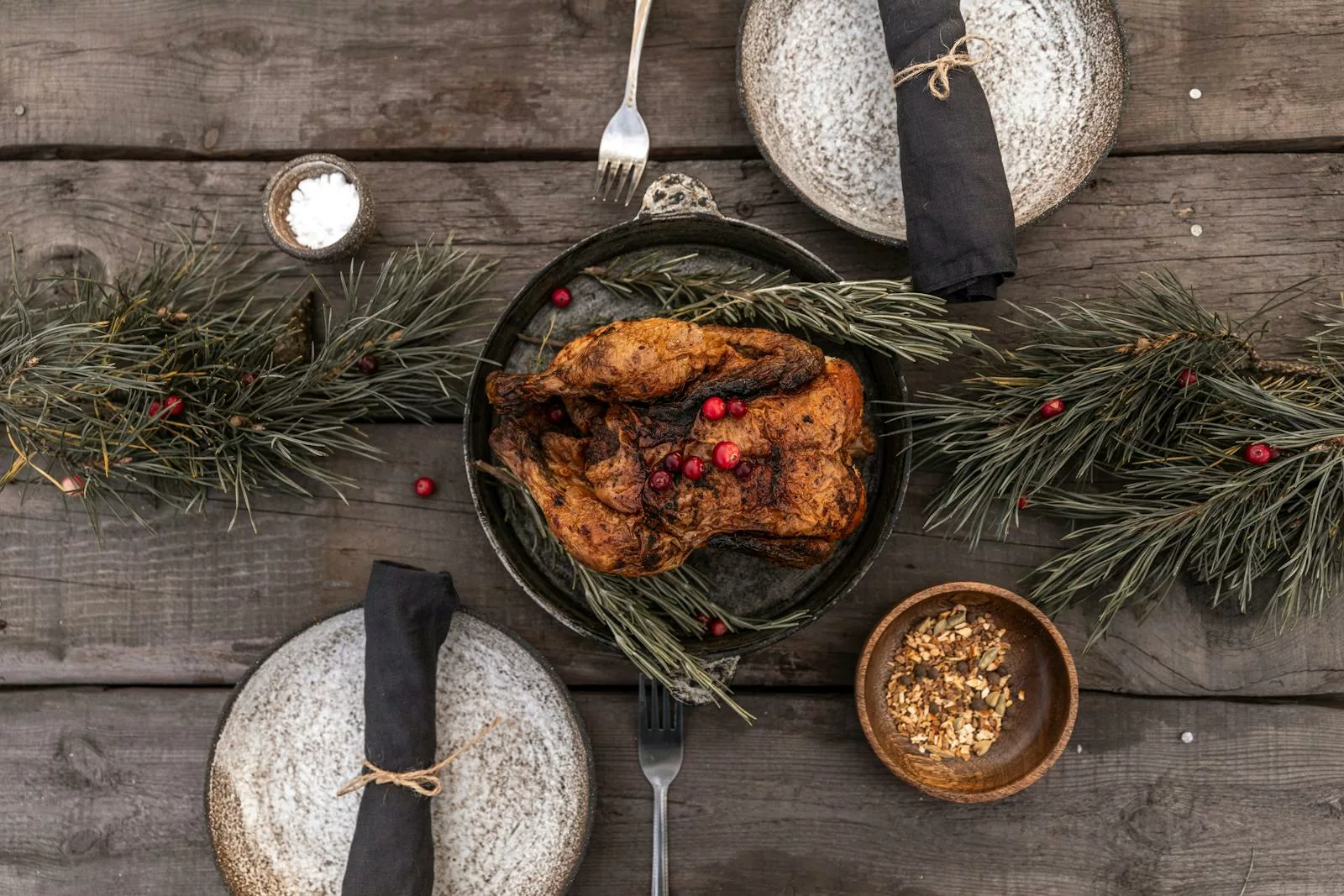 Elegant holiday table setup with roasted turkey and pine decoration.