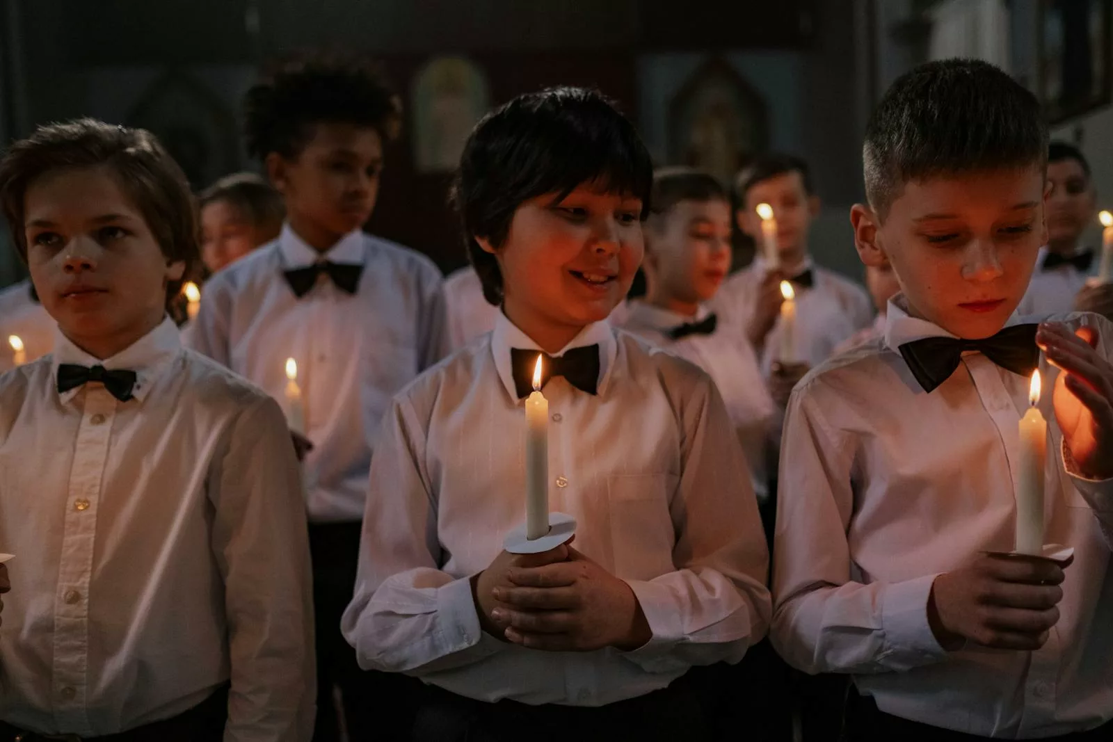 Children in formal white shirts holding candles during an indoor choir performance, fostering togetherness.