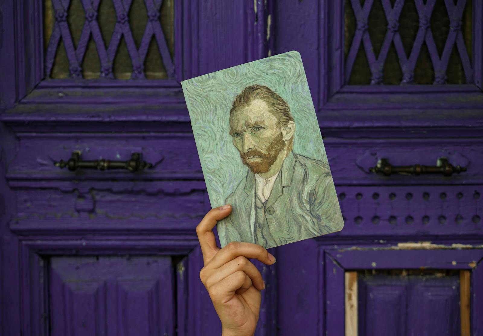A hand holding a Van Gogh self-portrait against a textured purple door background.