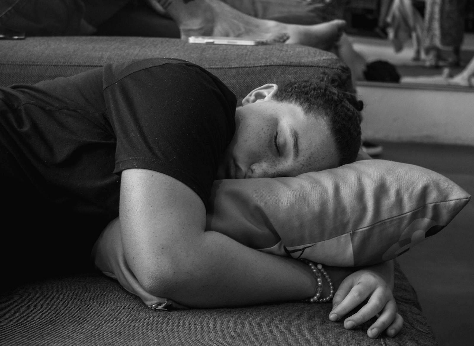 A person peacefully sleeping on a sofa, resting their head on a pillow in a black and white setting.