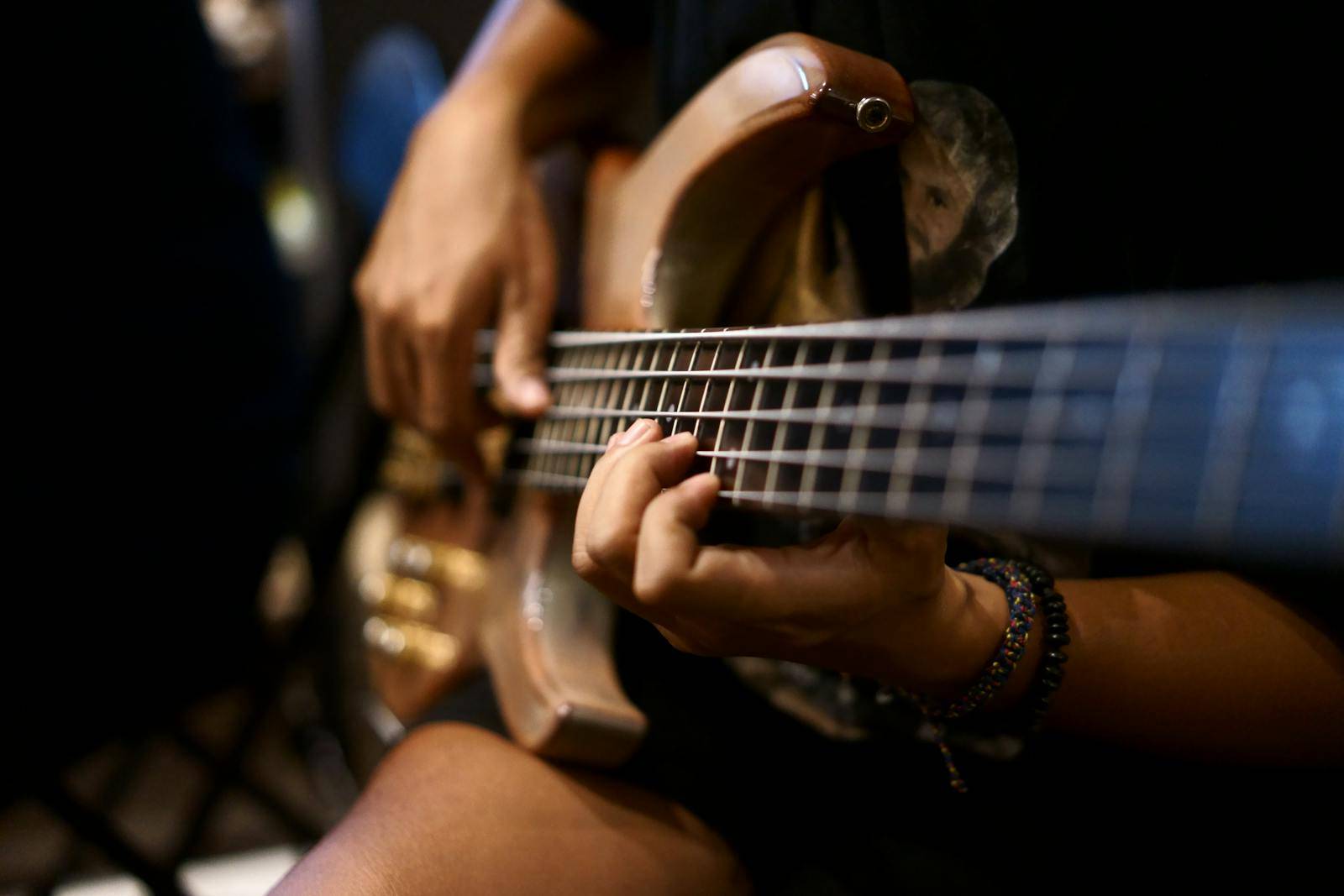 Detailed view of hands playing a bass guitar in a dimly lit setting.