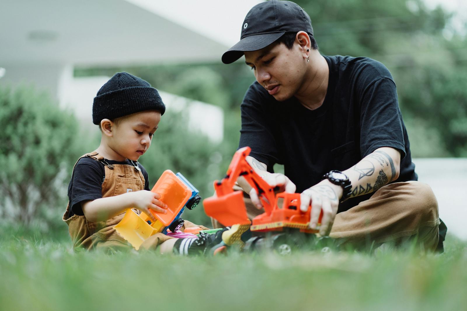 Father and son bonding time in the garden playing with colorful toy trucks, enjoying a sunny day.