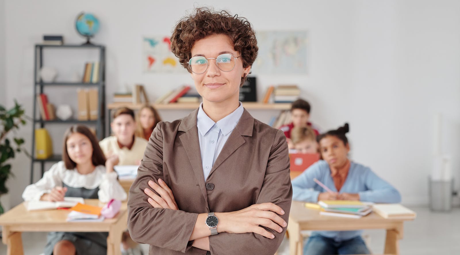 A confident teacher stands in front of students in a classroom setting.