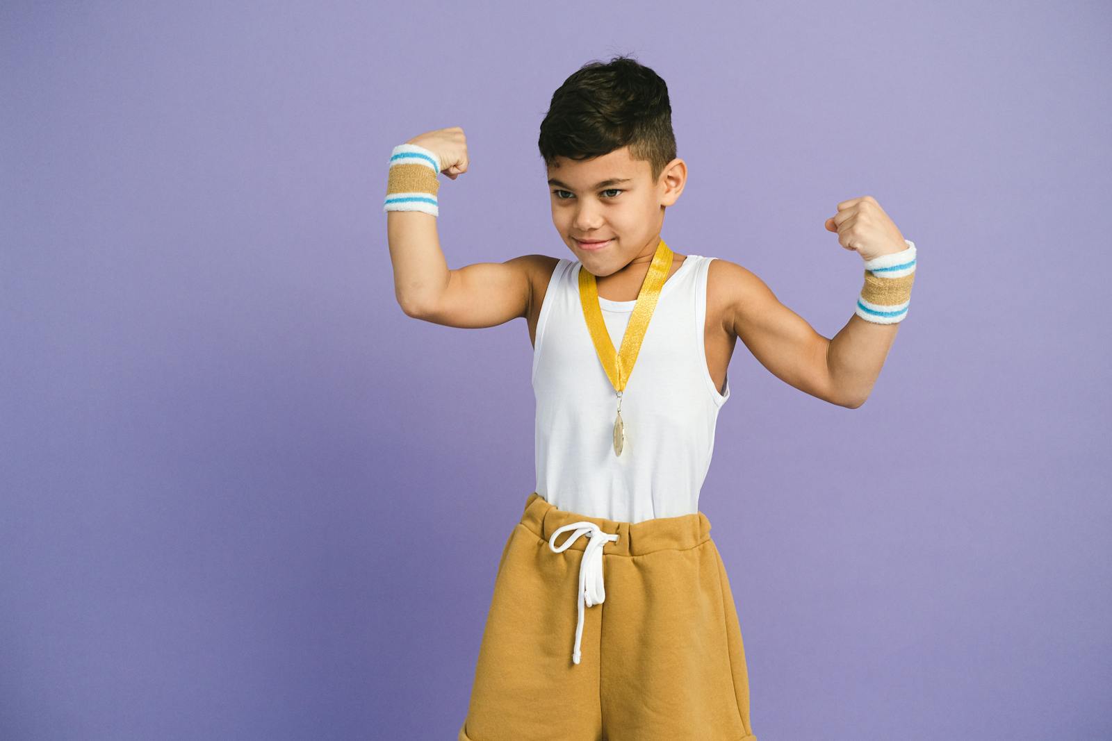 Young boy confidently flexes muscles with medal and sportswear. Perfect for themes of achievement and confidence.