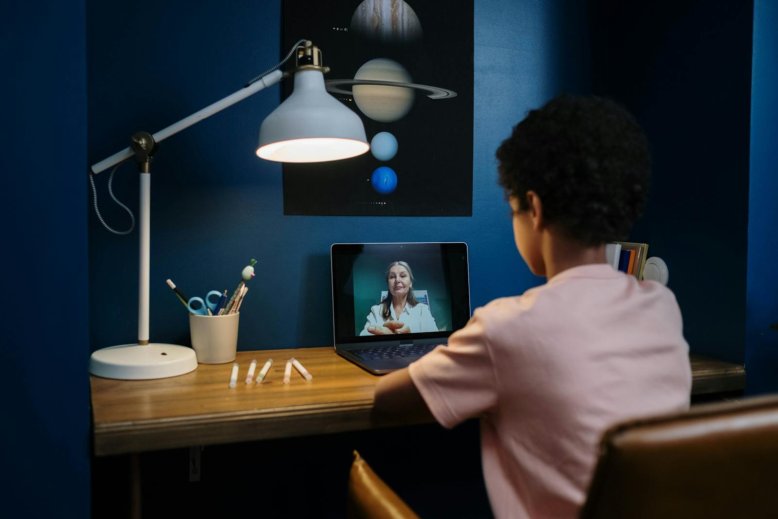 A young student engaged in an online with a teacher, sitting at a desk with a laptop.
