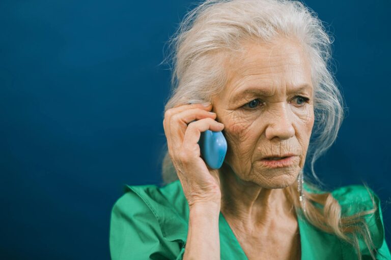 Senior woman with gray hair talks on mobile phone against a blue background.