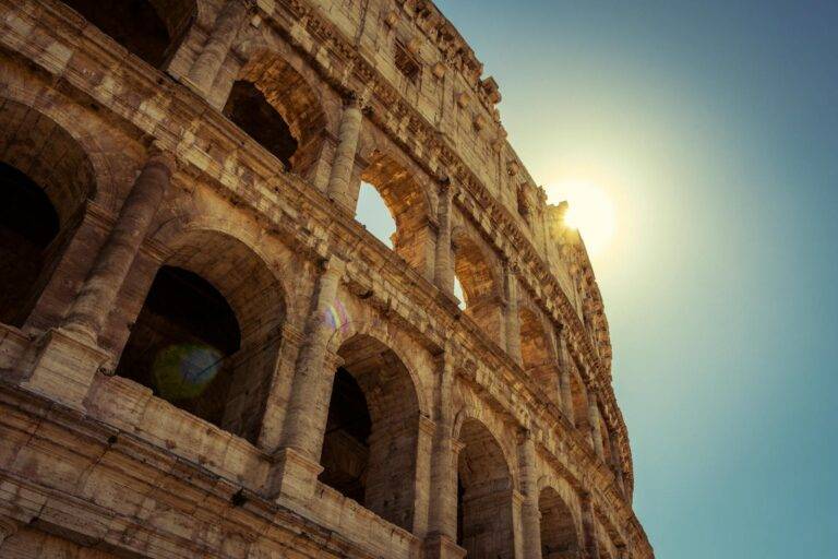 Low angle view of the Colosseum in Rome with sunlight shining through arches.