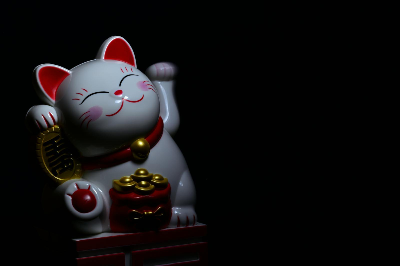 A ceramic Maneki Neko, or lucky cat, figurine symbolizing good fortune, with a dark background.