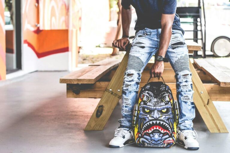 Edgy urban fashion photoshoot featuring ripped jeans and a bold graphic backpack.