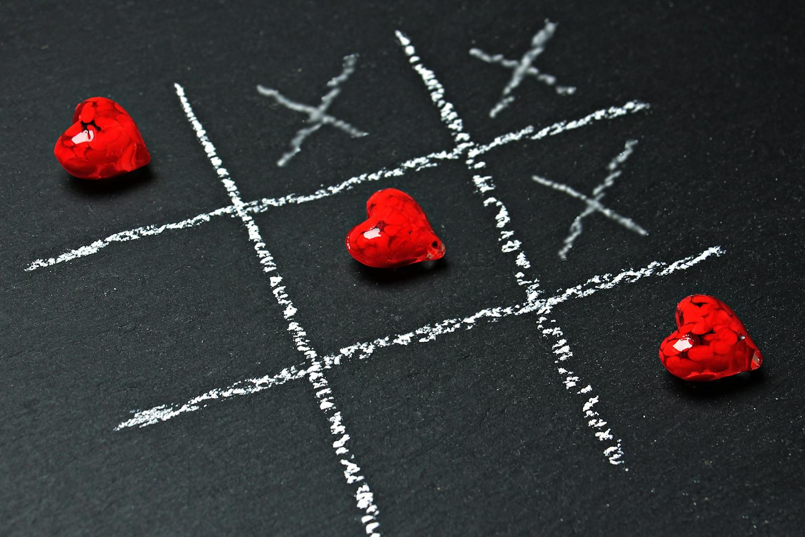 A passionate twist on tic-tac-toe with red heart pieces on a chalkboard grid.