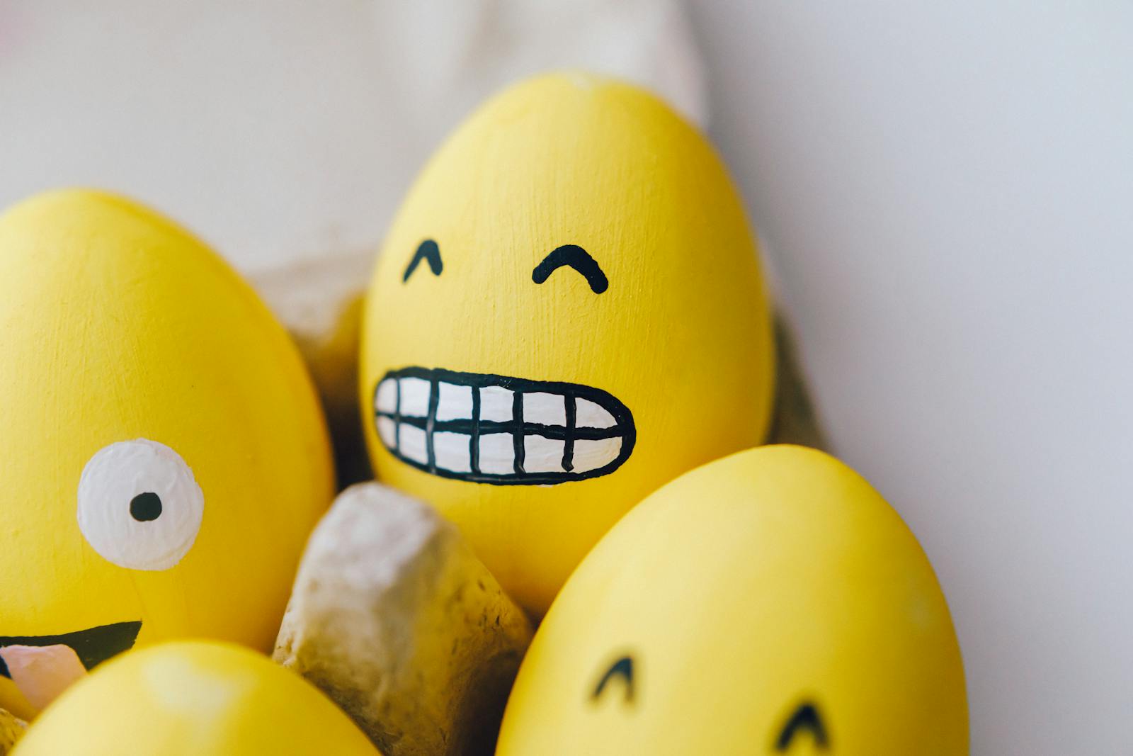 Vibrant yellow Easter eggs decorated with playful emoji faces in an egg carton.