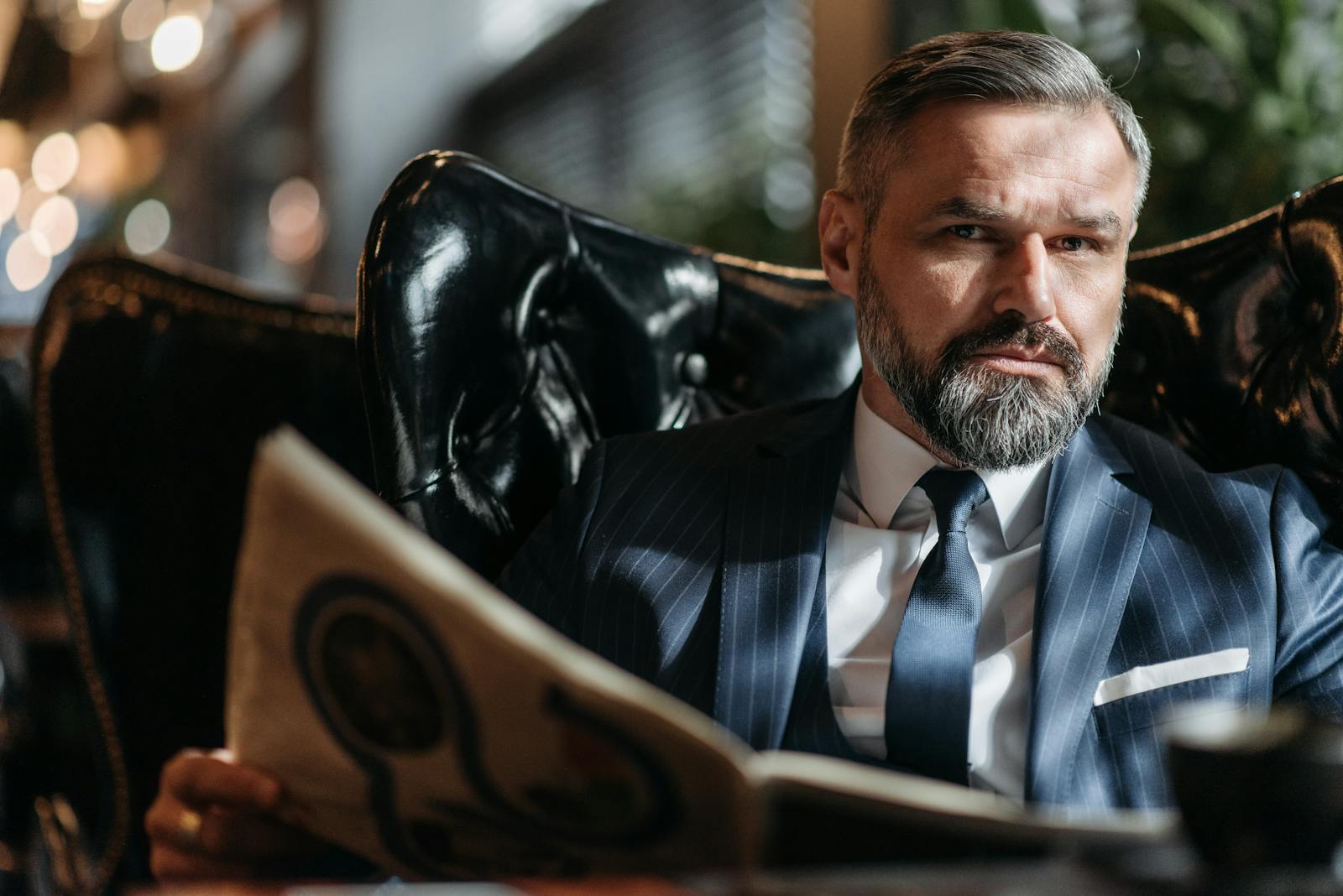 Stylish businessman with a beard reading a newspaper indoors.