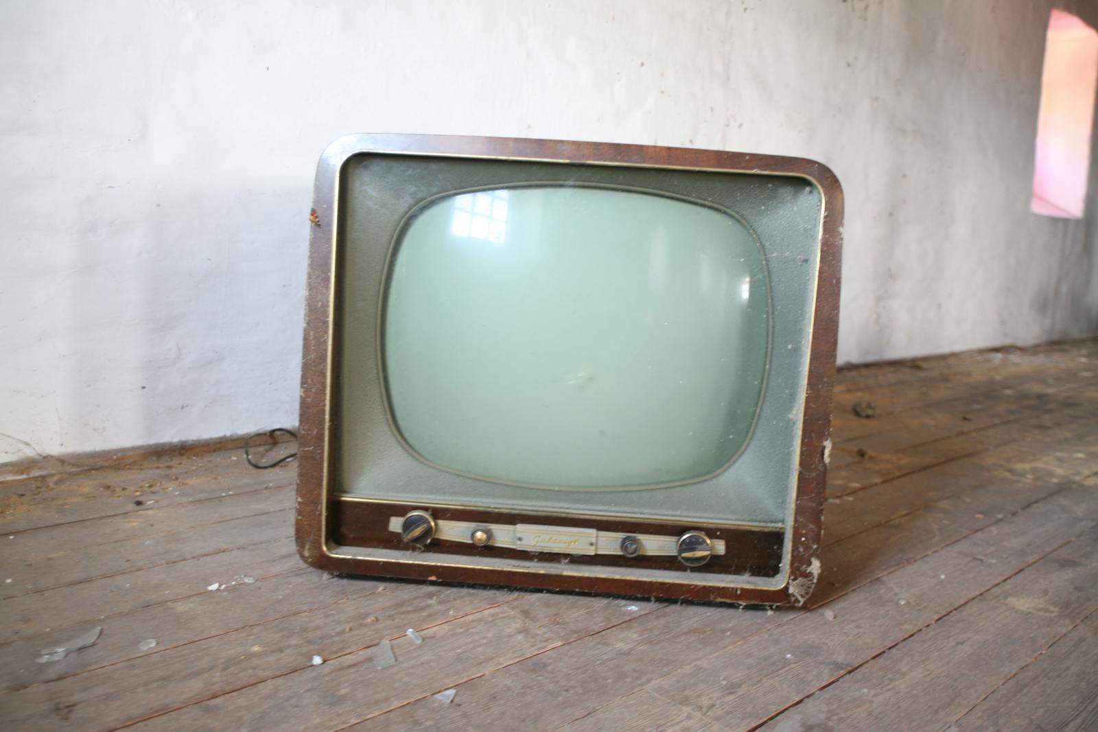 Vintage wooden television sitting on a dusty, rustic wooden floor in an abandoned room.
