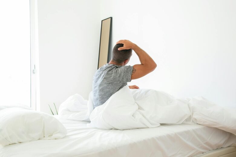 A man stretches in bed during a bright morning, starting his day.