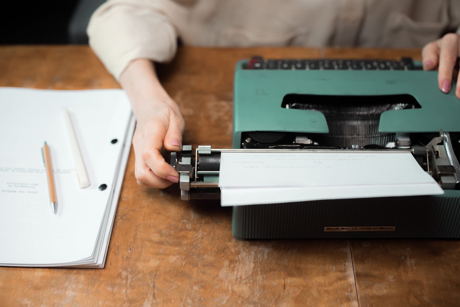Close-up of hands typing on a vintage green typewriter with papers on a wooden desk.