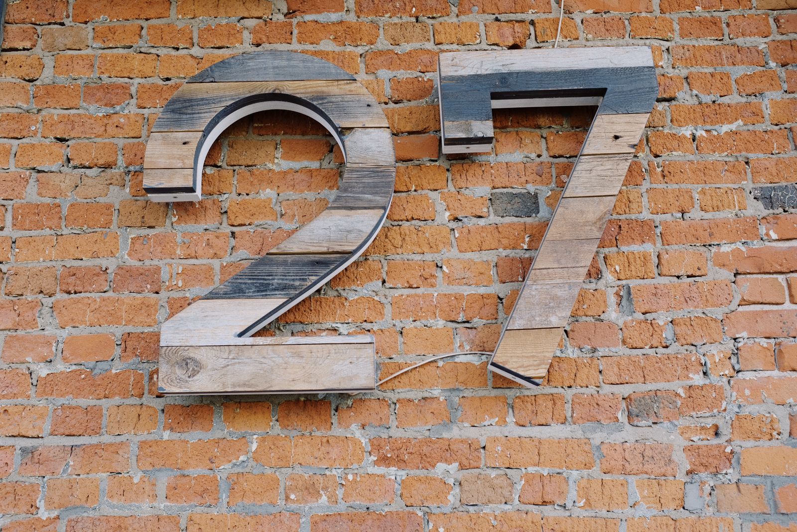 Big wooden sign of number 27 hanging on shabby brick wall of modern building on street in city