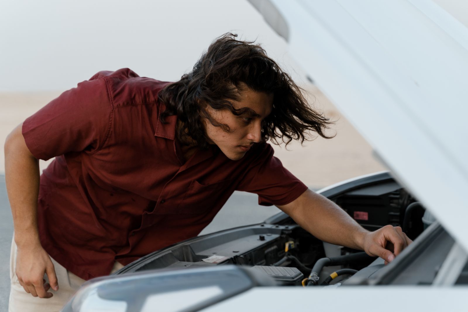 Person checking under the hood of a car for maintenance outdoors on a bright day.